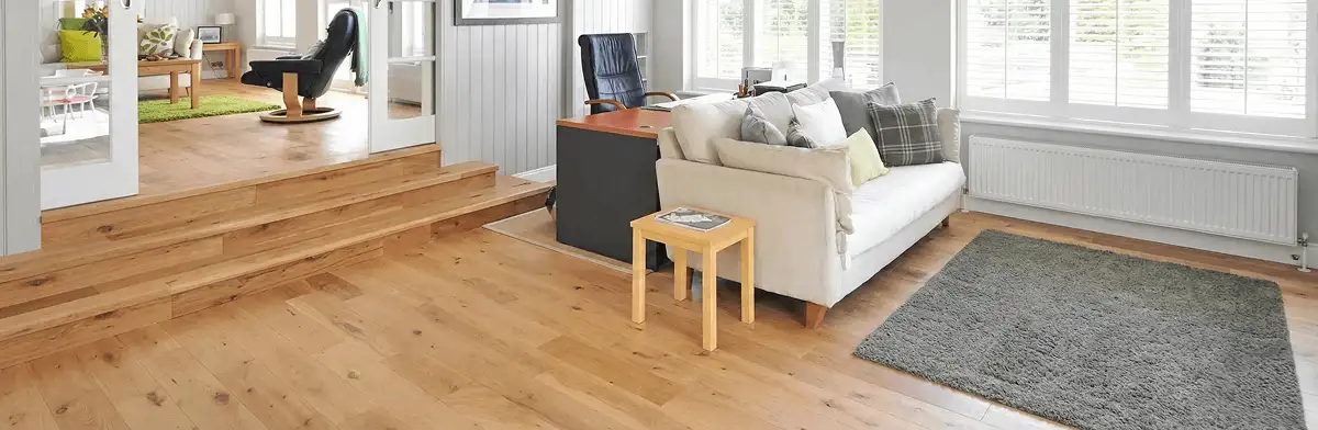 A modern living room with professionally installed laminate flooring, a beige sofa, a small side table, a gray rug, and large windows with white shutters in Raleigh, NC